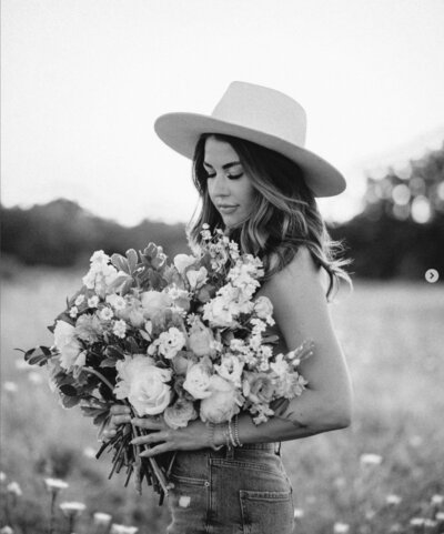 Woman wearing hat holding large flower bouquet in field