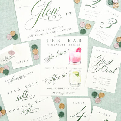 Collection of wedding day paper, day-of details, including wedding signature drink sign, guest book sign, table numbers, wedding place cards, wedding escort cards, and wax seals