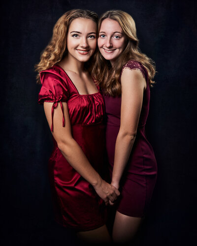 Blonde sisters wearing red-dresses holding hands and smiling