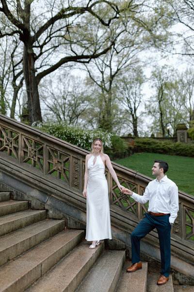 Engaged couple embracing in Central Park, NYC, with lush greenery background, by Hallie Noel Photography