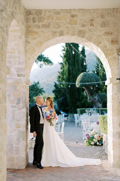 Bride and groom sharing a kiss under a stone arch during their elegant outdoor wedding, captured by a wedding photographer in Toronto