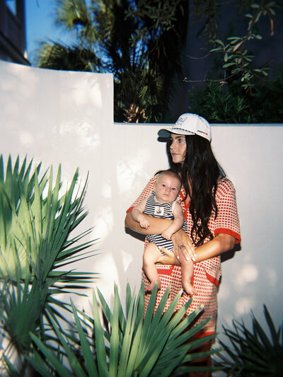 Film photo of mom in red sweater set holding her baby in front of a white wall