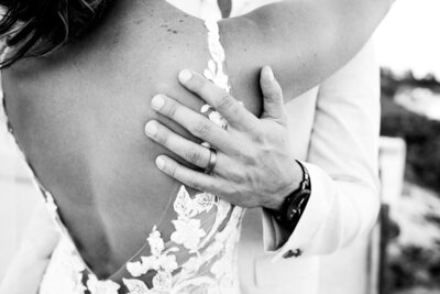 closeup of bride's dress details and groom's wedding ring embracing his wife.
