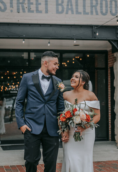 Bride and groom smiling outside wedding venue with bouquet