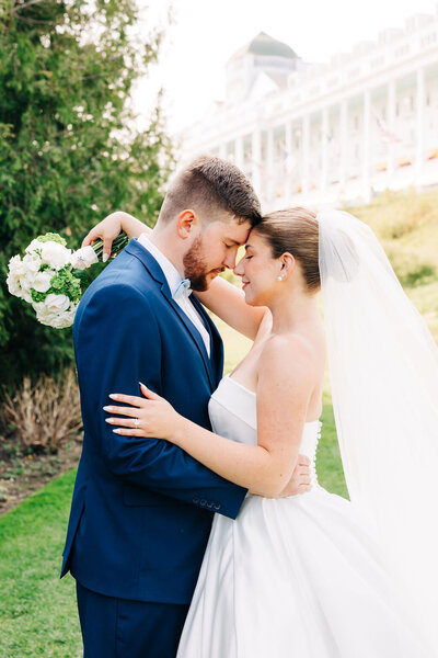 Couple embracing in wedding attire in front of greenery and The Grand Hotel