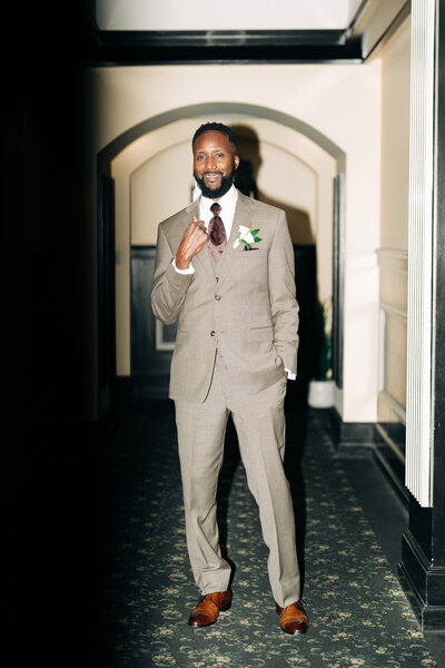 a groom waits in the hall in his tan tux