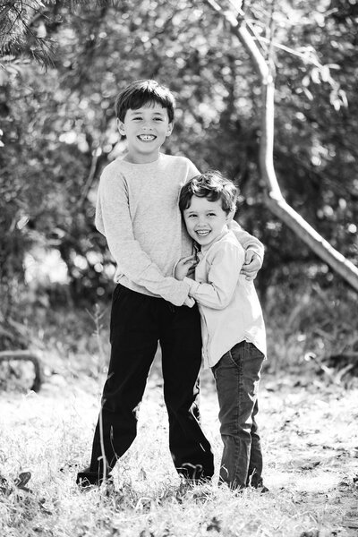 Two boys hug while smiling in their backyard