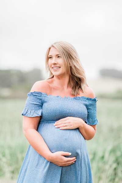 Expectant mother wearing a blue dress as she stares out into the distance imagining what it will be like to hold her baby boy for the first time.