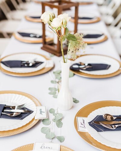 rustic wedding tablescape with gold chargers, white plates, and navy blue napkins coordinated by cait and co events