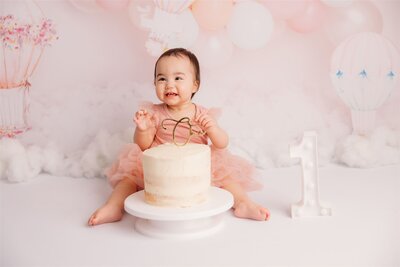 Ilena sitting with her first birthday cake during her cakemash photoshoot with michelle kelly photography in her auckland photography studio