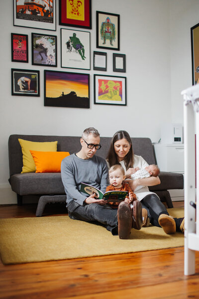family reading book on nursery floor during Toronto Newborn session