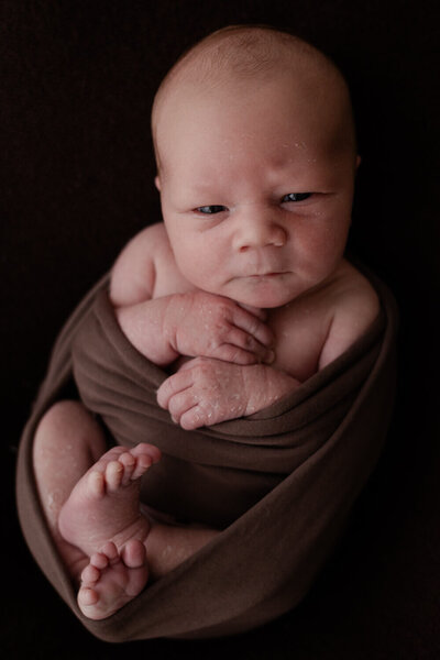Baby in een ontspannen pose, gefotografeerd tegen een zachte bruine achtergrond. Professionele newborn shoot aan huis.