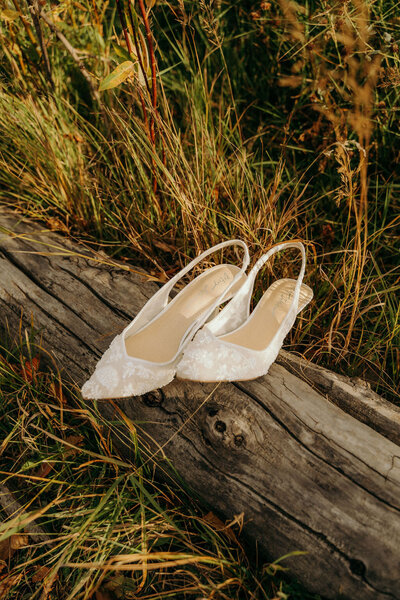 bridal shoes sitting on a fallen log in the grass