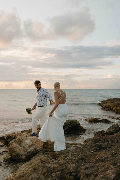 Candid moment of couple holding hands on coastal rocks with ocean in the background.