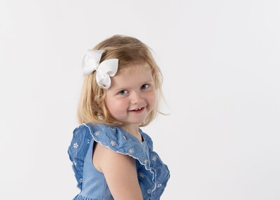 A young girl looking back over her shoulder with a big smile posing for her school portrait.