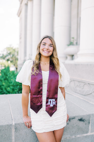 Girl in a white dress and a Texas A&M stole standing in front of a building