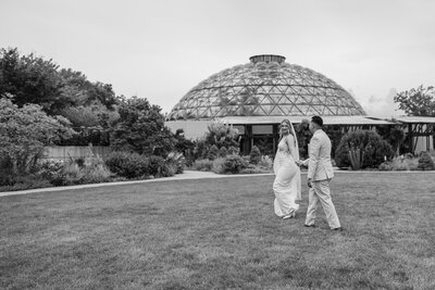 A bride leads her groom through a botanical garden in Des Moines, IA. Black & white photo by Claire Katan Creative.