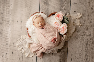 Newborn baby girl with hands on face laying on a pink background