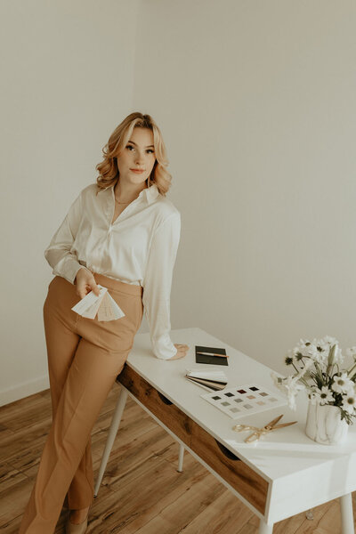Woman in camel colored pants standing by desk
