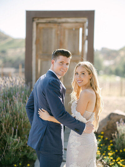 Bride with natural dewy makeup featuring soft bronze eyeshadow, fluttery lashes, and nude lips, styled with loose waves and middle part for a romantic outdoor vineyard wedding 