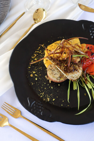 Artfully plated gourmet fish entrée with roasted vegetables and microgreens on black plate, showcasing exceptional culinary offerings at Ashlar Ottawa for intimate celebrations and private events