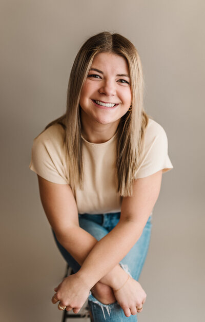 Young female posing for a headshot and branding session smiling at camera on a neutral tan backdrop