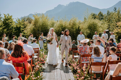 A bride and groom wearing a yellow and green puffy jacket hold each other on top of Rainbow Glacier in Whistler. There is snow all around and blue skies.