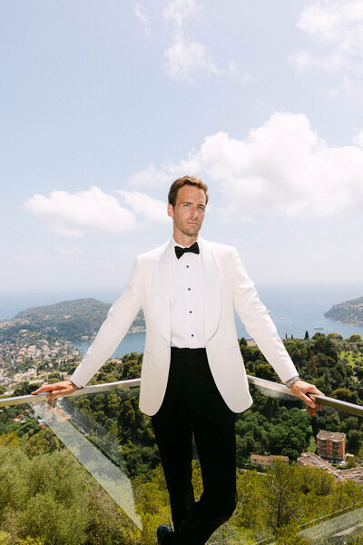 Groom in white tuxedo posing at the balcony of Bride and her 18 bridesmaids that wear coloful fashionable dresses at Villa Ephrussi. 