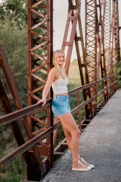 Teenage girl leans against bridge, smiling for the camera.