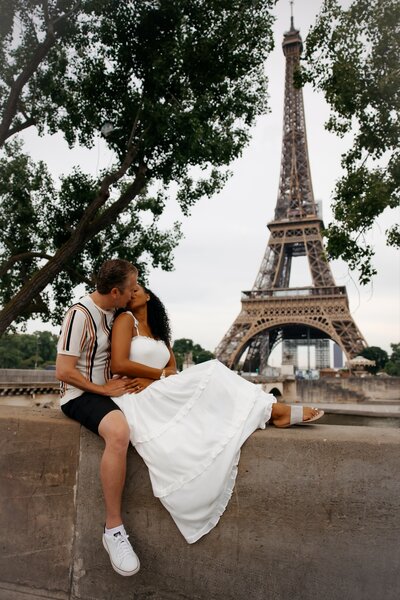 Couple embraces while sitting on a while with the Eiffel tower in the background