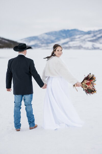 Bride and groom walk across frozen Colorado lake.