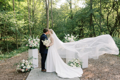 A bride and groom kissing at the end of the ceremony isle at Bear Ridge Destination. The location is a woodland dream filled with luscious trees and beautiful sunlight.  