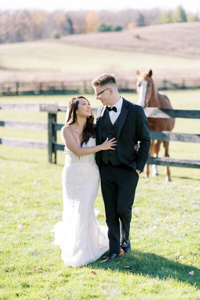 Bride and groom walking hand in hand near paddock with horses at Caledon wedding venue, captured by Toronto photographer