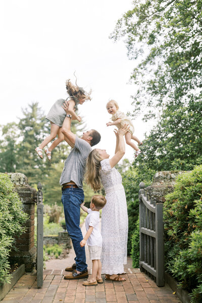 Mom and dad throw two of their children in the air as their third child looks on during family portrait session