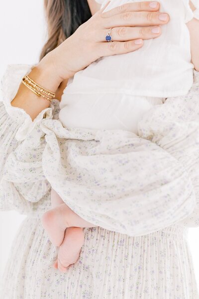 A woman holding a baby in a white dress at a Charlotte portrait session.