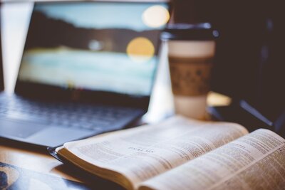 closeup-shot-open-bible-with-blurred-laptop-coffee