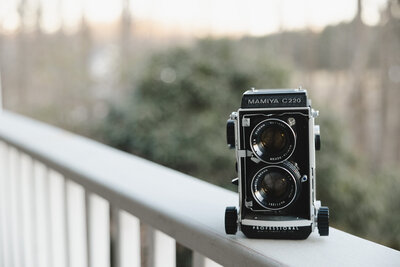 A vintage camera sitting on the railing of a porch 