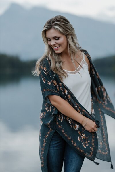 Cochrane Couples and Lifestyle photographer smiles while looking down and spinning  while standing in front of a mountain lake