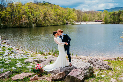 Eloping couple embracing by a scenic lake with spring greenery at a West Virginia elopement