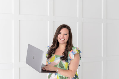 woman standing by a white wall holding a computer taking the what's missing in your marketing quiz