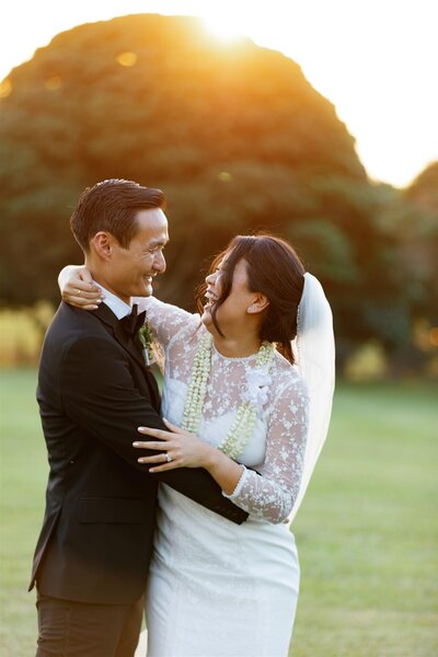 A wedding couple with their arms around each other laughing at sunset 