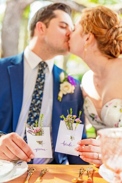 Bride and groom kiss while holding white name cards