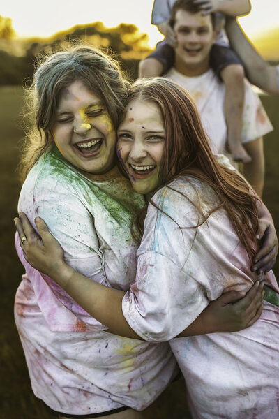Two sisters hug each other during a family paint war at a sunset family session in Shawnee, Kansas