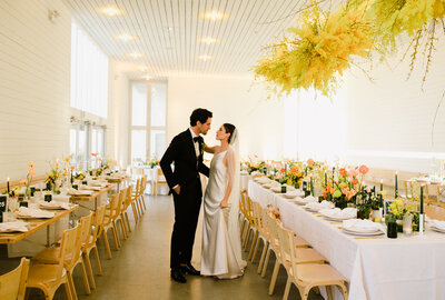 Bride and groom standing inbetween tables at colorful wedding reception with bright yellow and orange florals at Prospect House Wedding