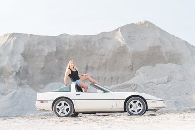 a girl posing while sitting on a Corvette
