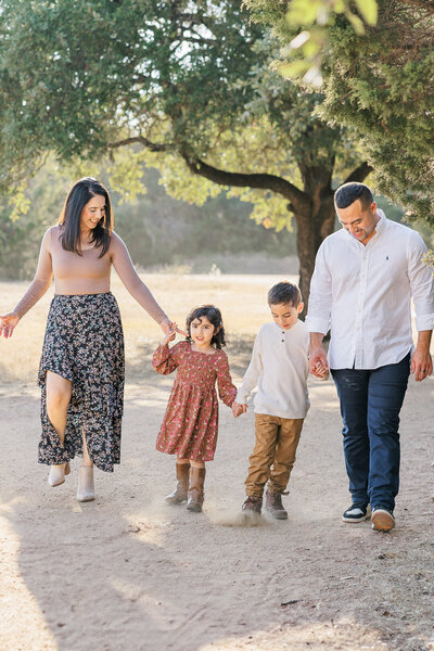 Two little boys stand on a sandy path holding hands for their family portraits in Austin, TX. They wear matching plaid shirts and blue jeans.