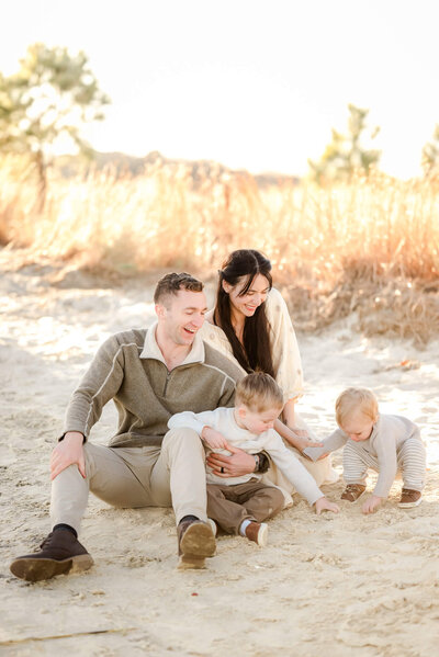 Justine Renee Photography captures a candid photo of a family playing in the sand. The two young boys dig in the sand while the mom and dad smile down at them.