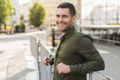 Smiling man standing near a city waterfront, representing confidence and relief after engaging in somatic therapy in Brooklyn.