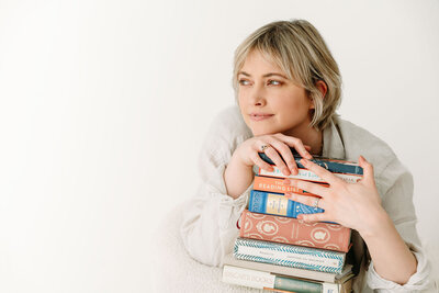 Een stapel boeken vastgehouden door Rosanne van Cruijningen, zelfstandig redacteur en schrijfcoach voor romanschrijvers.