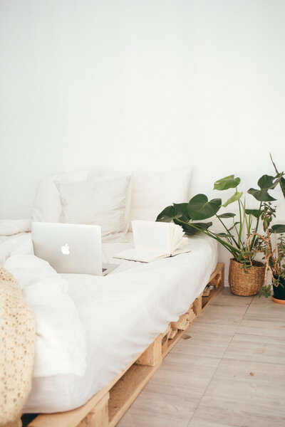 Laptop sitting on bed with white sheets next to book and plant
